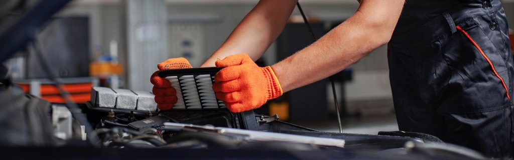 A person wearing orange gloves is replacing an air filter in a car engine.