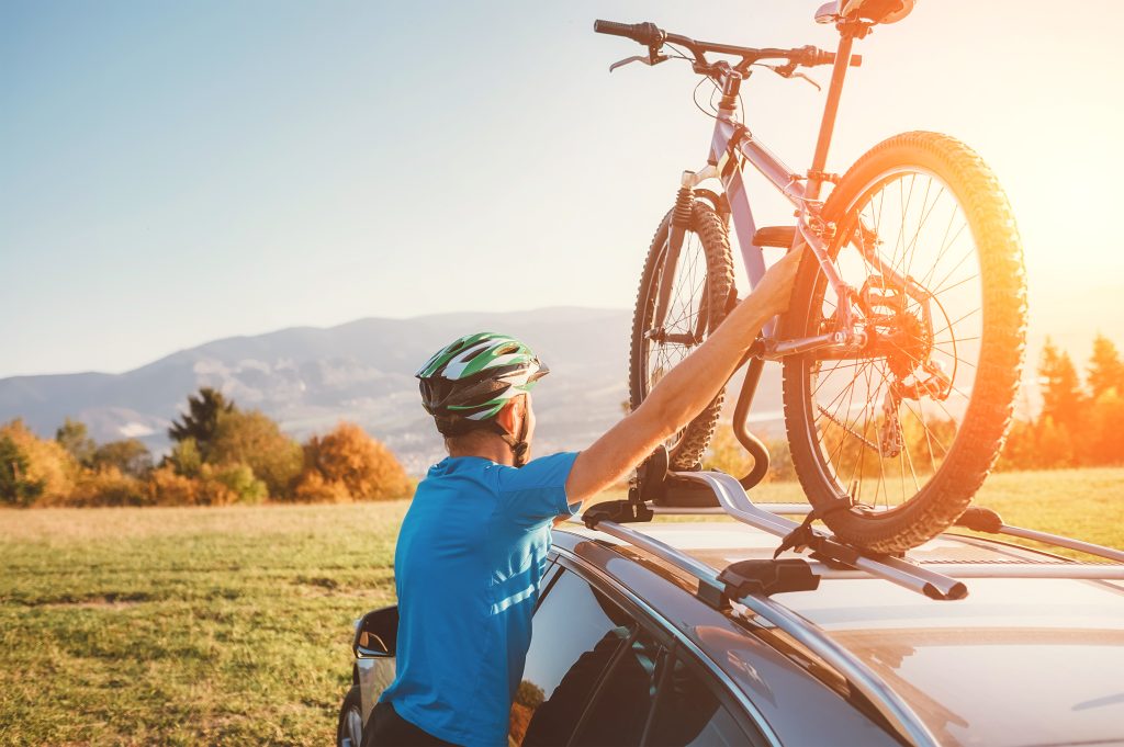 A person loading a mountain bike onto a car's roof rack during sunset
