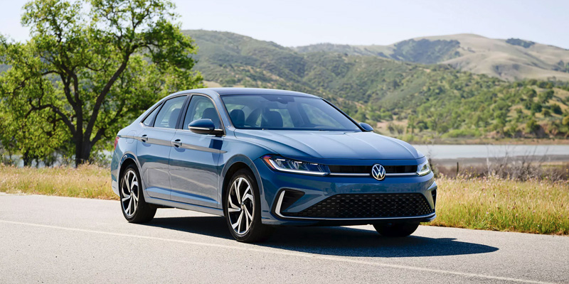 Blue Volkswagen Jetta sedan parked beside a scenic lakeside road.