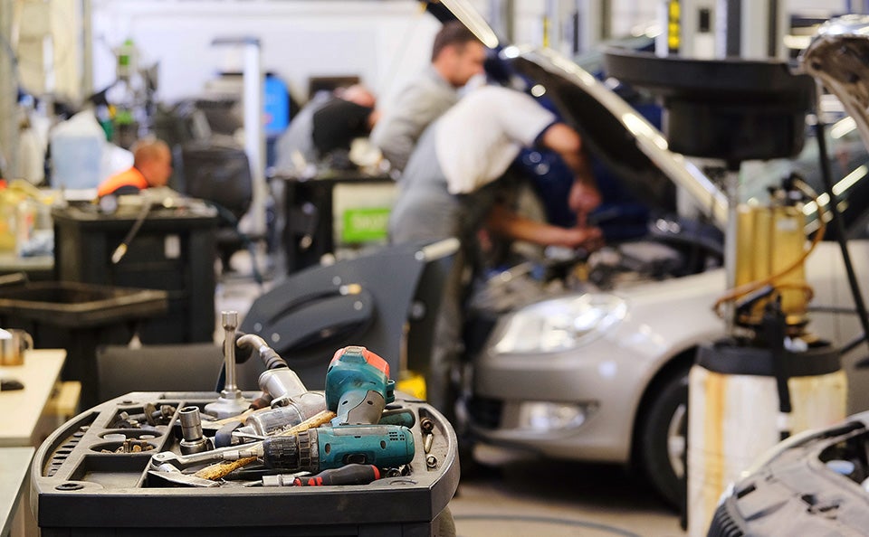 Mechanics servicing a car in an auto repair shop with tools in the foreground.